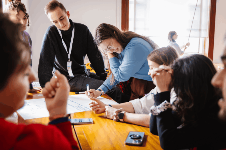 Grupo de estudiantes internacionales colaborando en un proyecto en el marco de una actividad Erasmus+, escribiendo ideas en una hoja grande durante una sesión participativa.