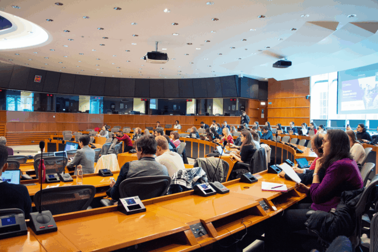European Parliament conference room filled with delegates attending an Erasmus+ policy discussion, featuring modern technology and international participants.