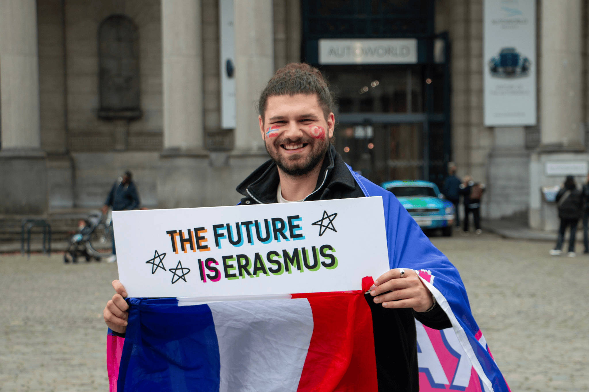 un estudiante universitario sostiene un cartel que dice «el futuro es erasmus» frente a un edificio de la Unión Europea