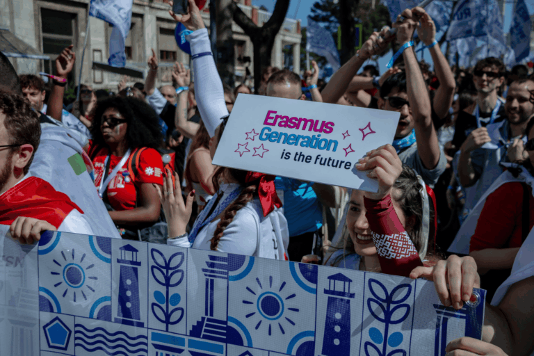 image of people during a flag parage smiling and having fun. there is one sign in the front that says: Erasmus generation is the future