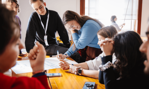 web10 Grupo de estudiantes internacionales colaborando en un proyecto en el marco de una actividad Erasmus+, escribiendo ideas en una hoja grande durante una sesión participativa.